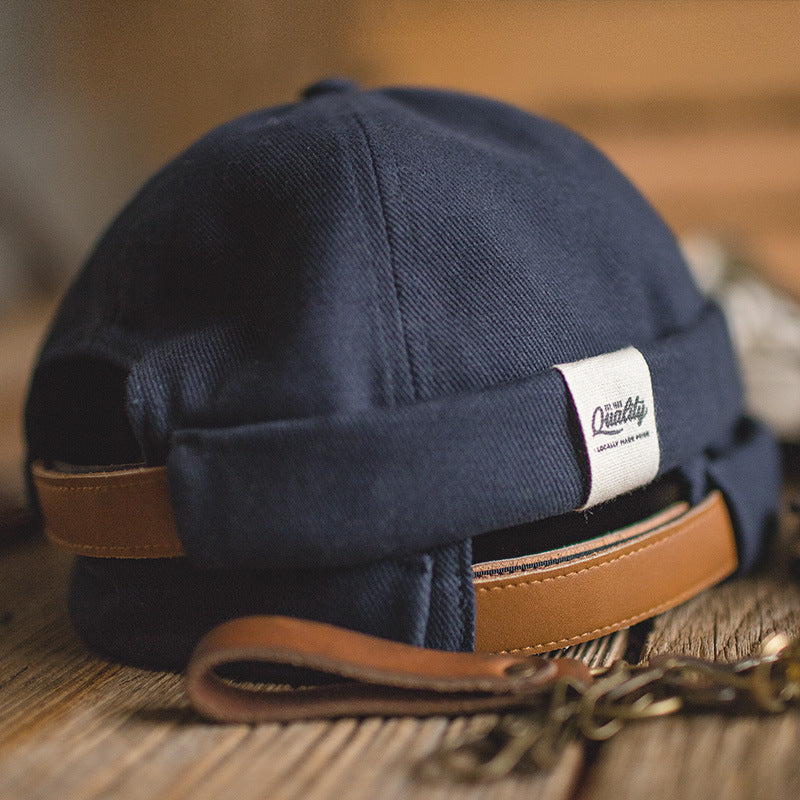 Close-up of a navy cotton docker hat featuring an open back, brown adjustable strap and white woven label