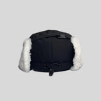 Adjustable ear flap cap in black, rear view with a black crown strap, toggle drawcord and white faux-fur panels
