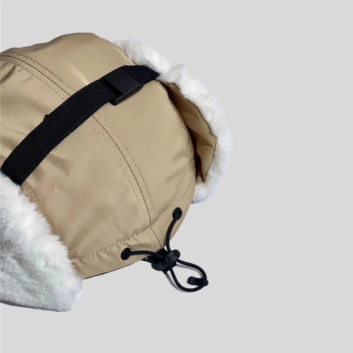 Adjustable winter cap in khaki, close-up of the crown buckle strap, rear eyelets and elastic toggle cord

