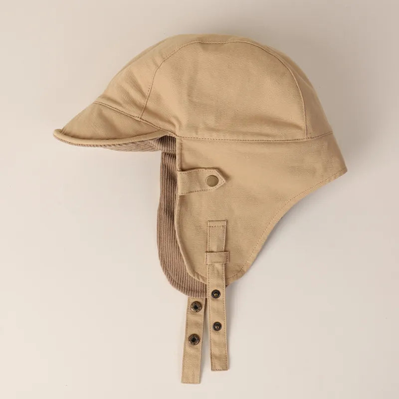 Beige ear flap cap side profile showing the short peak, extended ear panels and adjustable snap straps.