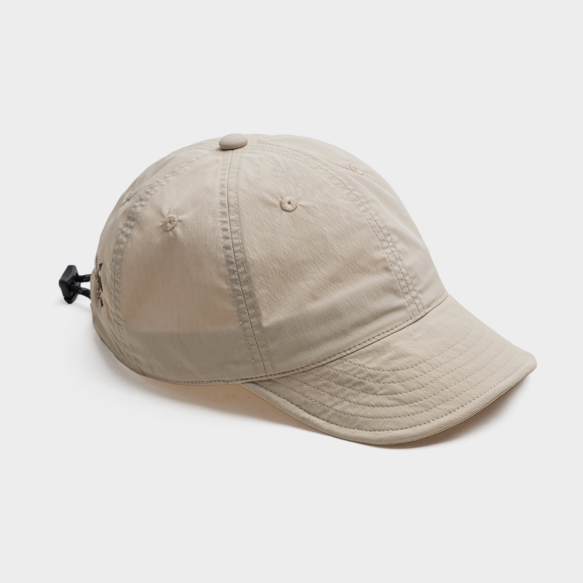 Beige nylon baseball cap with a curved stitched brim, panelled crown and rear drawcord adjustment