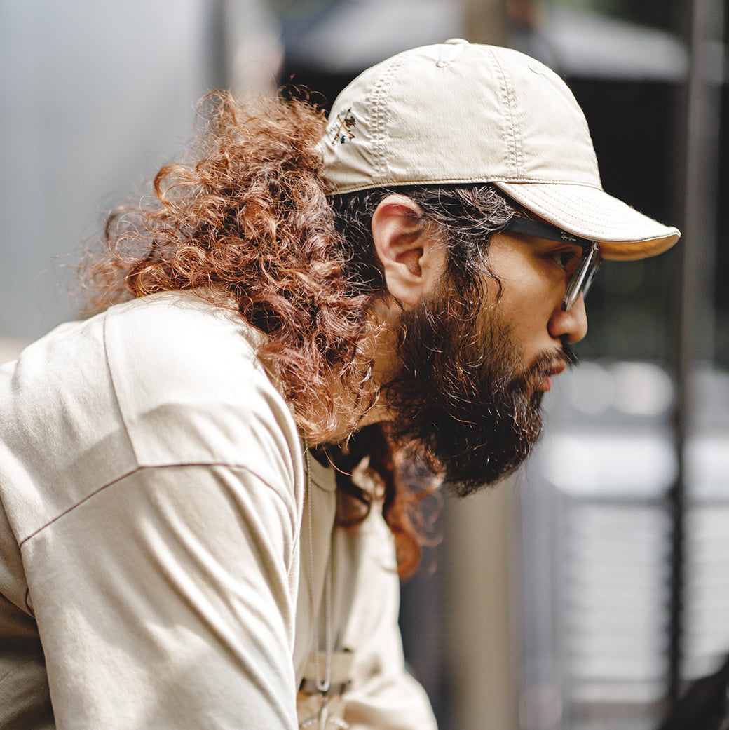 Man wearing a beige nylon baseball cap with a curved brim for a relaxed casual streetwear look