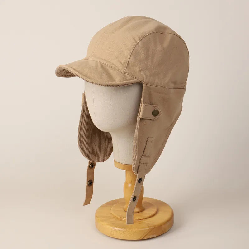 Beige winter cap with ear flaps shown front-on, featuring a short visor and long protective side panels.