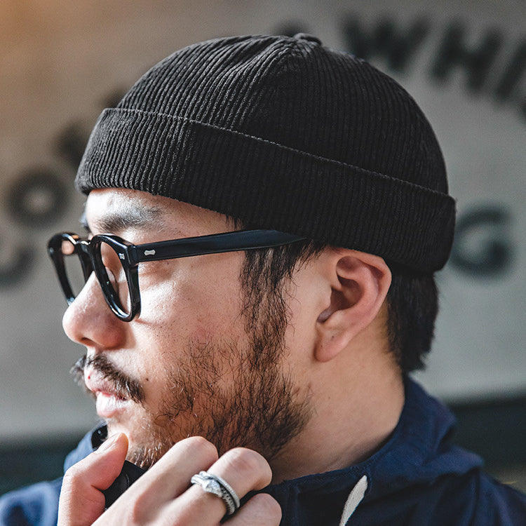 Side profile of a man wearing a black cotton corduroy skull cap with a low-profile brimless design
