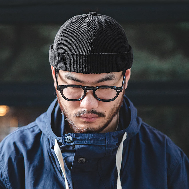 Front view of a man wearing a black cotton corduroy docker cap with a clean rolled-edge design