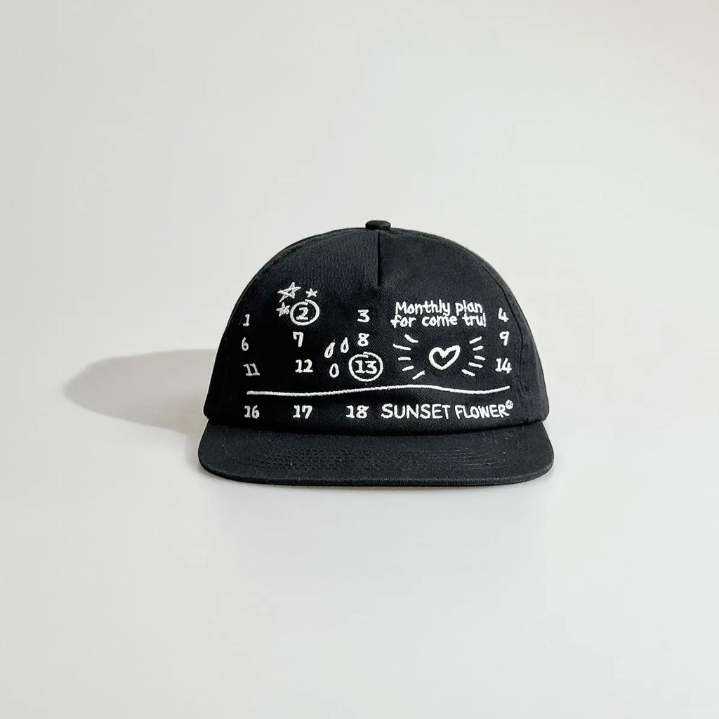 Front view of a black cotton baseball cap with a flat brim and graphic front design for casual everyday wear.
