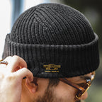 Man wearing a black cotton ribbed beanie with a wide folded cuff and small woven side label