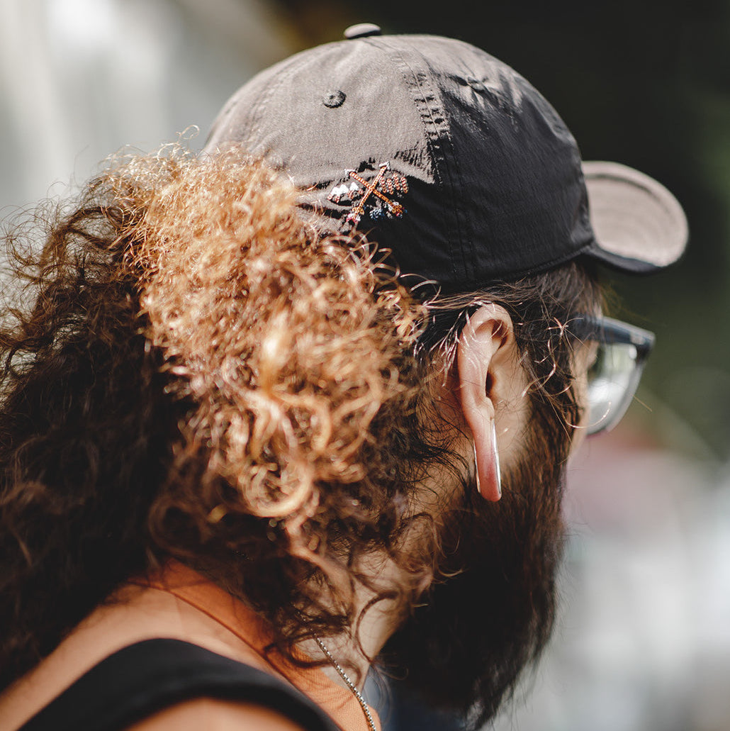 Black nylon baseball cap worn from the rear side, featuring a small outdoor-inspired embroidered graphic