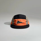 Front view of a black and orange five-panel cap with leopard print side panels, a triangle logo patch and a stitched flat brim.