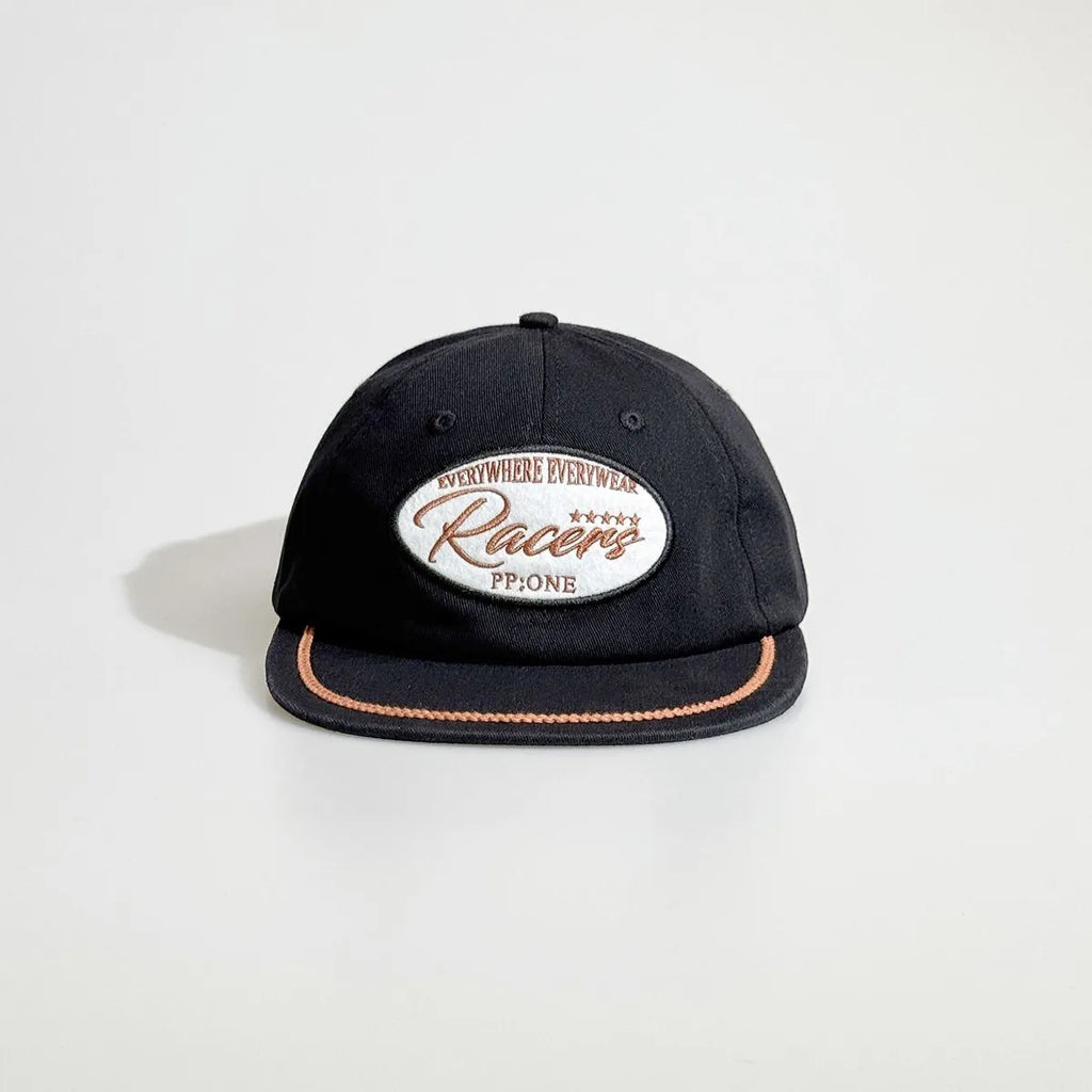 Front view of a black baseball cap with an oval racing patch, tan rope trim and a flat brim for casual streetwear.