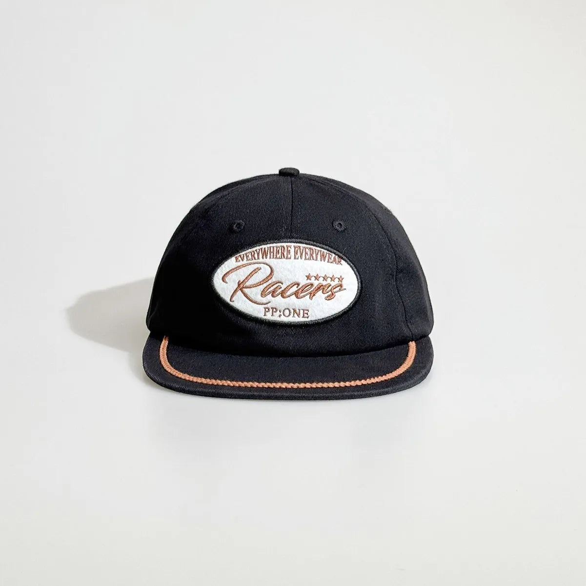 Front view of a black baseball cap with an oval racing patch, tan rope trim and a flat brim for casual streetwear.