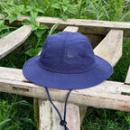 Indigo blue boonie hat shown front-on outdoors, with a low crown, broad stitched brim and matching chin cord.