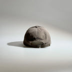 Back view of a brown adjustable baseball cap with embroidered lettering, ventilation eyelets and a metal buckle strap.