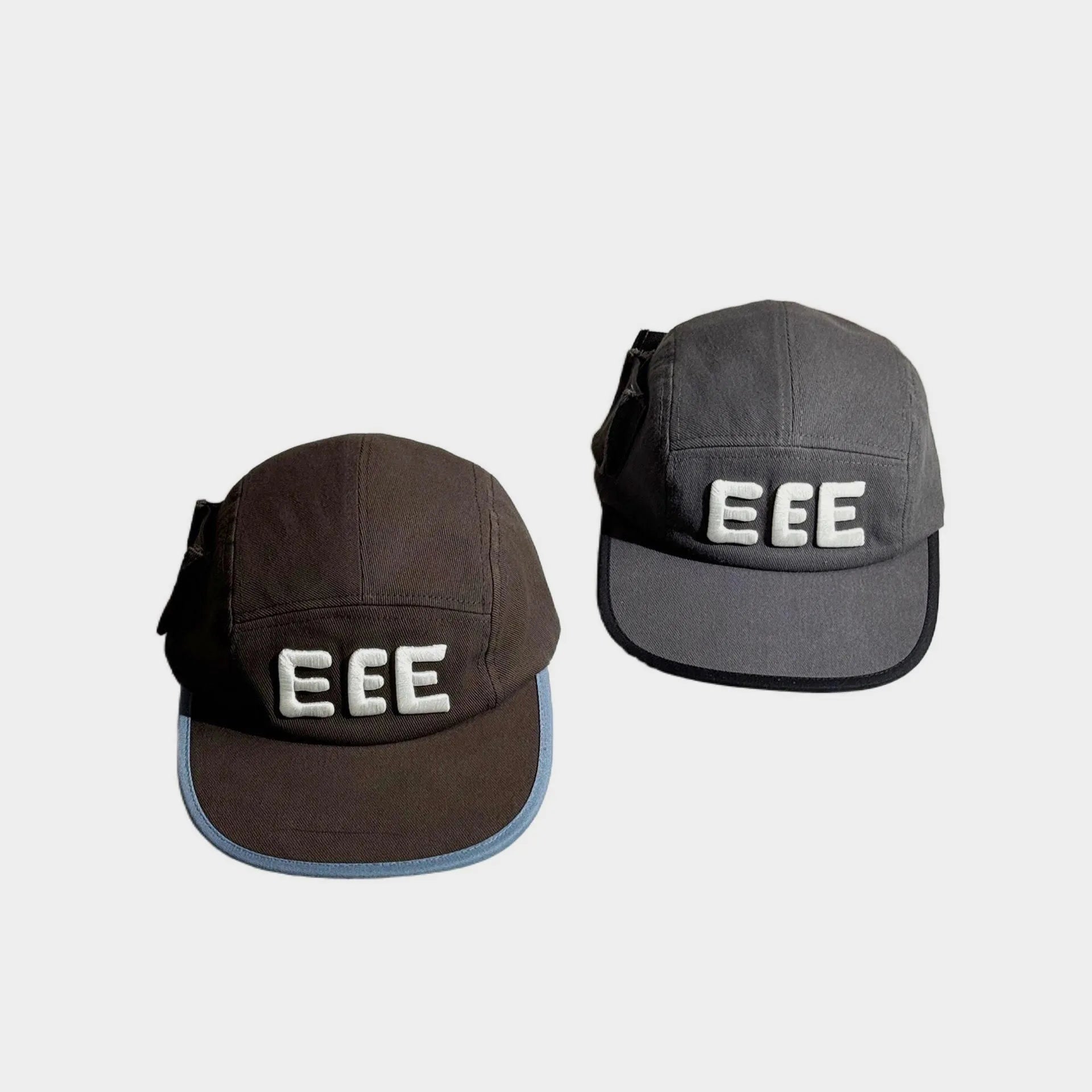 Front view of brown and grey five-panel caps with raised white EEE embroidery, flat brims and contrasting edge trim.