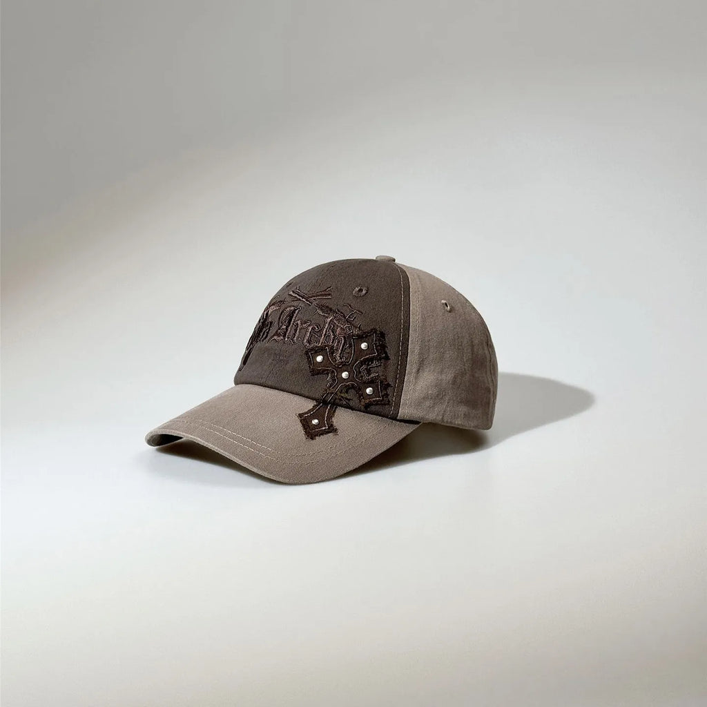 Brown two-tone gothic baseball cap featuring dark embroidered lettering, stud details and a curved visor.