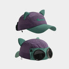 Purple cat ear baseball cap with teal green accents, shown from the curved brim and decorative goggle sides.
