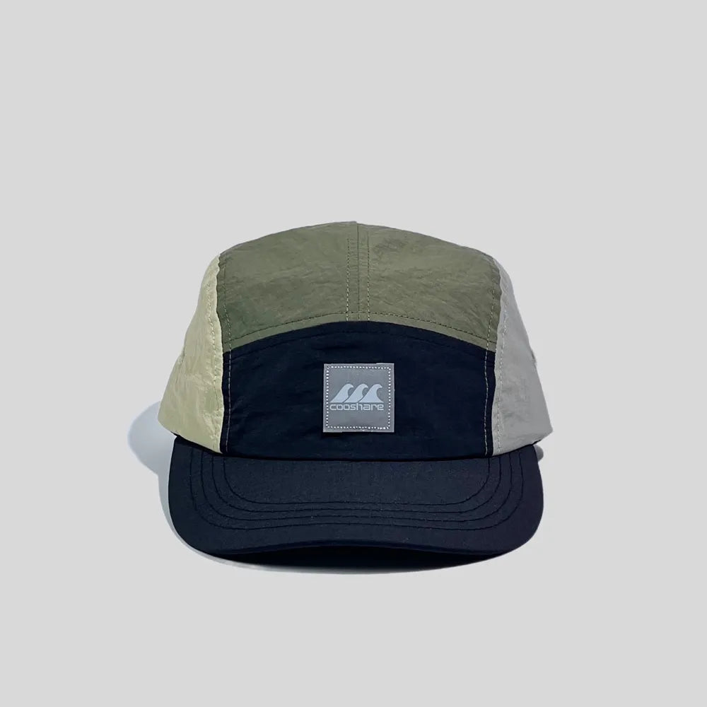 Colour block five panel cap in olive green, beige, light grey and navy, front view with a logo badge and curved brim