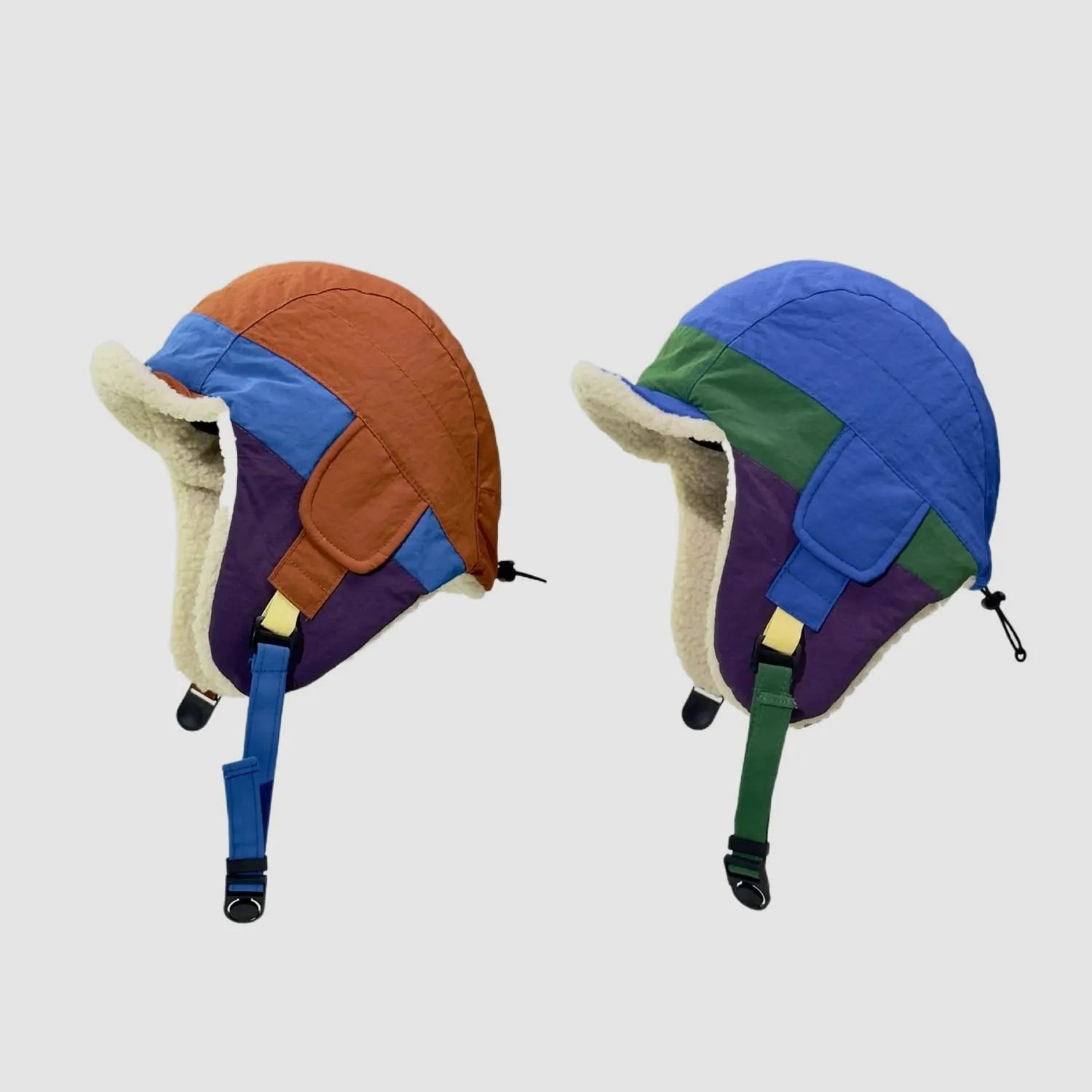 Colour block trapper hat shown in orange-blue and blue-green variants with padded ear flaps and curved peaks.