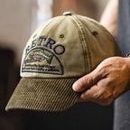 Hand holding a khaki cotton cap with a curved corduroy brim, RETRO text and multicolour fish embroidery