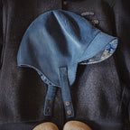 Flat lay of a navy cotton corduroy ear flap cap with patterned under-brim and metal snap straps