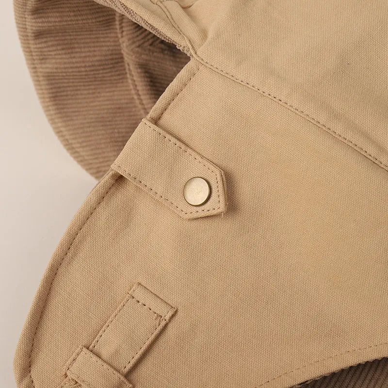 Beige ear flap cap close-up highlighting the metal press stud, stitched tab and structured side panel.