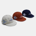 Embroidered baseball caps displayed in light grey, rust red and navy colour options with cartoon and text graphics
