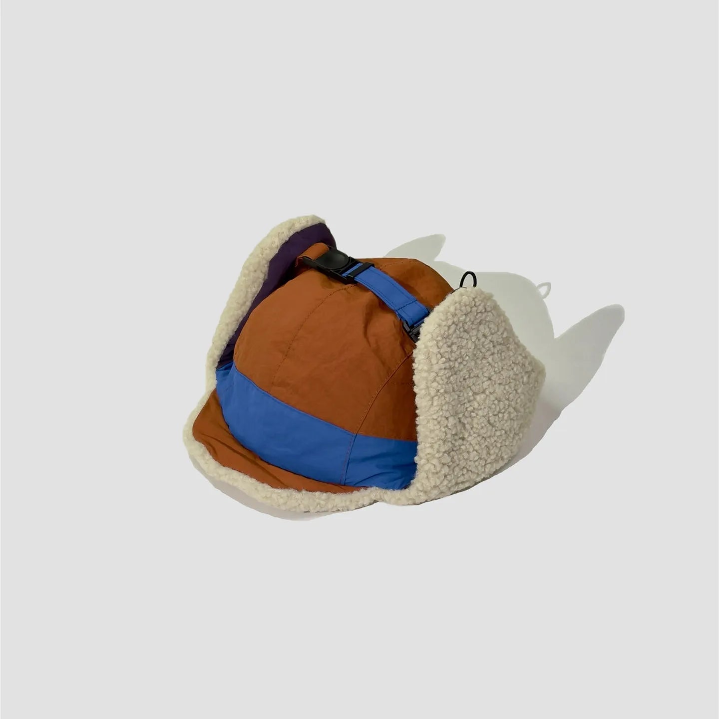 Orange and blue winter trapper hat rear view with cream fleece ear flaps and adjustable chin strap.