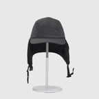 Black fleece-lined winter cap front view with ear flaps down, curved peak and hanging buckle straps.