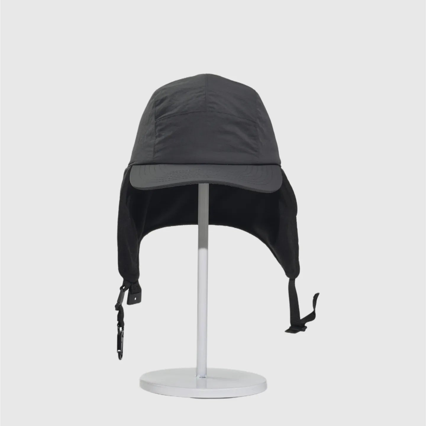 Black fleece-lined winter cap front view with ear flaps down, curved peak and hanging buckle straps.