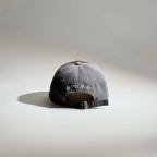 Back view of a grey adjustable baseball cap with embroidered lettering, ventilation eyelets and a metal buckle strap.