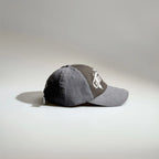 Side view of a grey two-tone baseball cap with gothic embroidery, contrast panels and an adjustable back strap.