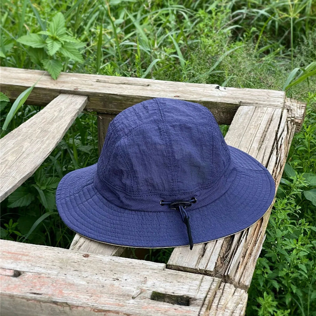 Indigo blue hiking sun hat on a weathered bench, its fine grid weave standing out against green foliage.