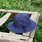 Indigo blue hiking sun hat on a weathered bench, its fine grid weave standing out against green foliage.