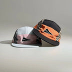 Front view of two color-block five-panel caps featuring leopard and zebra print side panels, contrast brims and triangle logo patches.