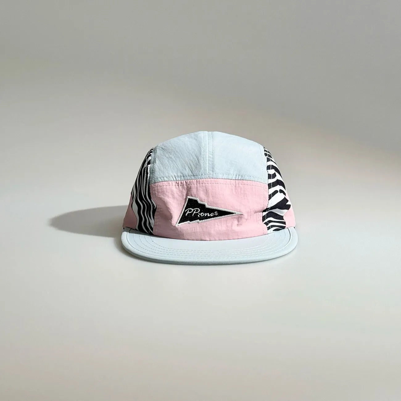 Front view of a light blue and pink color-block five-panel cap with zebra print side panels, a triangle logo patch and flat brim.
