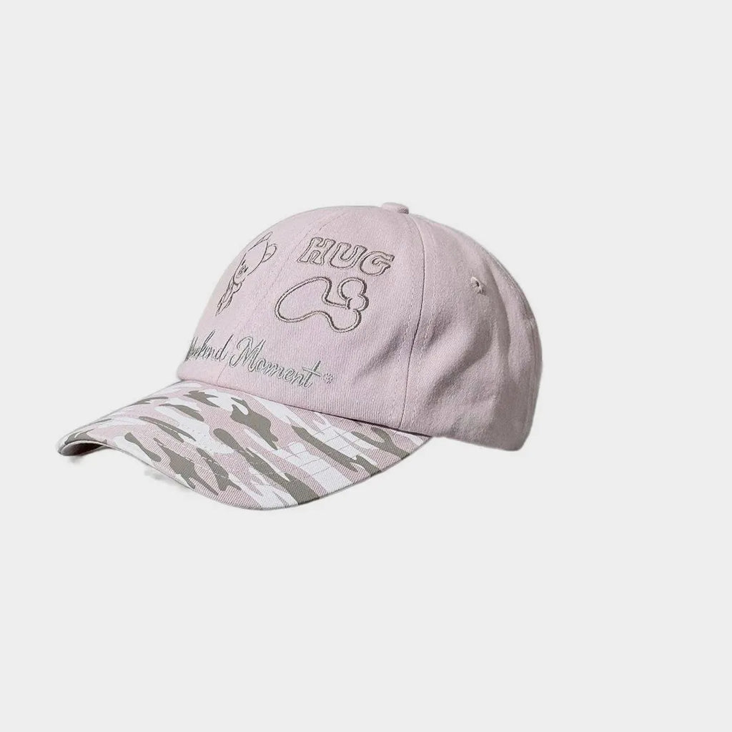Side view of a light pink baseball cap with bear, HUG and bone embroidery and a pink camouflage curved brim.