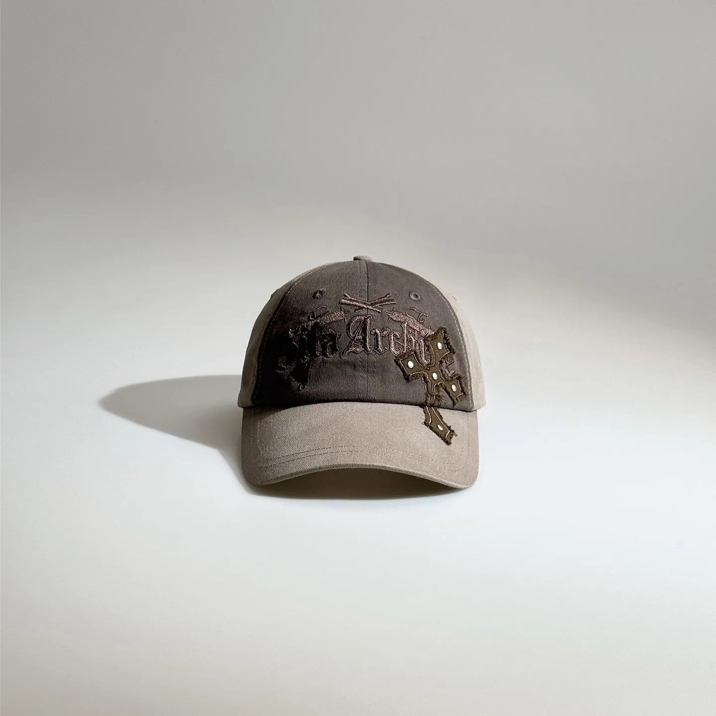 Front view of a men's brown embroidered baseball cap with gothic graphics, contrast panels and metal stud accents.
