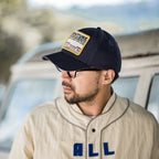 Side view of a man wearing a navy Adventure patch baseball cap outdoors