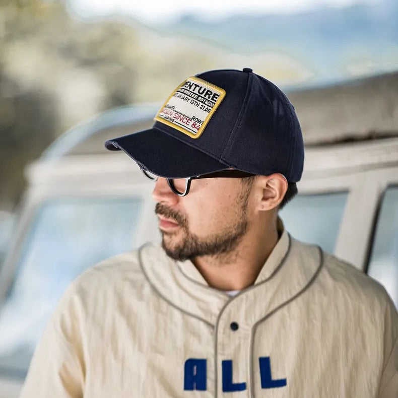 Side view of a man wearing a navy Adventure patch baseball cap outdoors