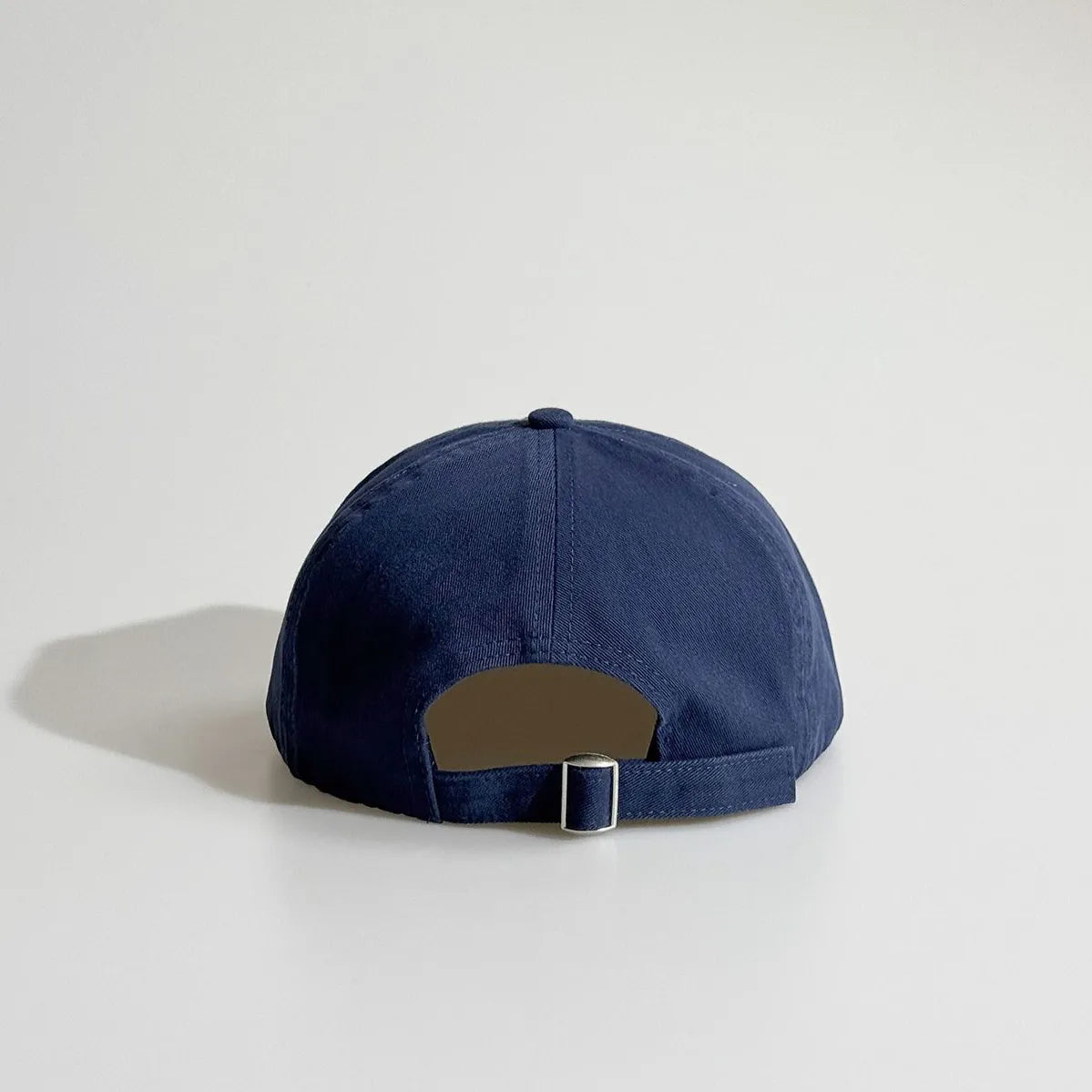 Back view of a navy dad cap with an open back and adjustable metal buckle closure.