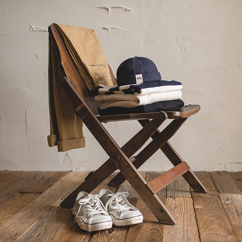 Navy cotton brimless cap styled with folded knitwear, casual trousers and canvas shoes for a vintage everyday look