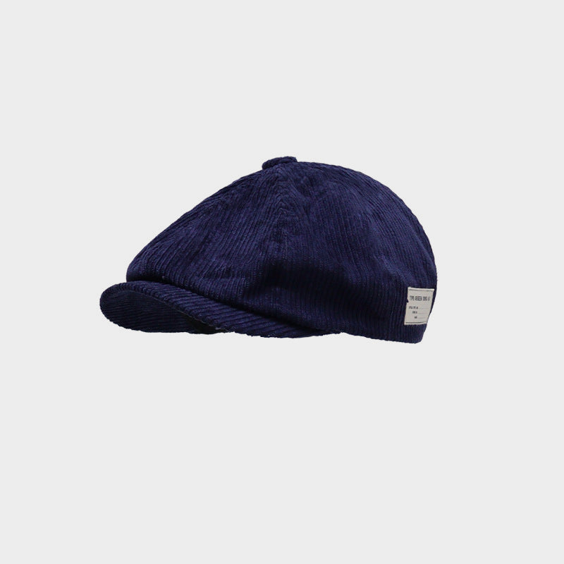 Navy corduroy newsboy cap in a three-quarter product view with ribbed panels, top button and short curved peak