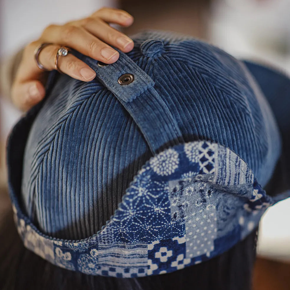Back detail of a navy cotton corduroy ear flap cap with patterned lining and snap-button strap