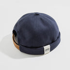 Navy cotton docker cap with a rolled cuff, white woven label and brown adjustable back strap