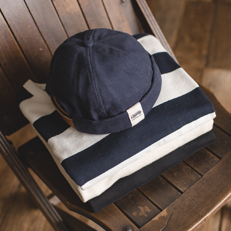Navy cotton sailor cap with a rounded panelled crown and rolled edge displayed on striped knitwear