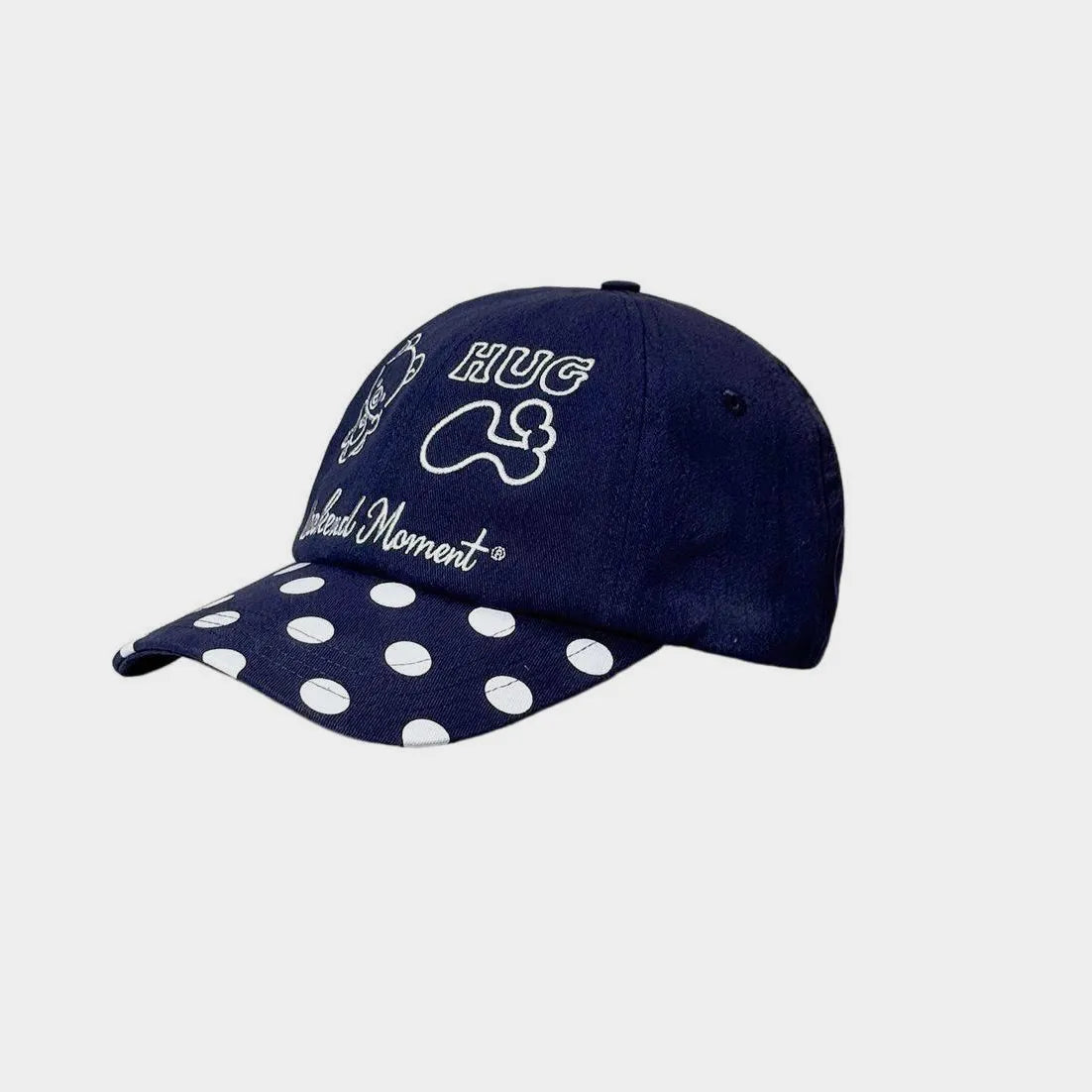 Angled view of a navy baseball cap with white bear, HUG and bone embroidery, Weekend Moment script and a polka dot curved brim.