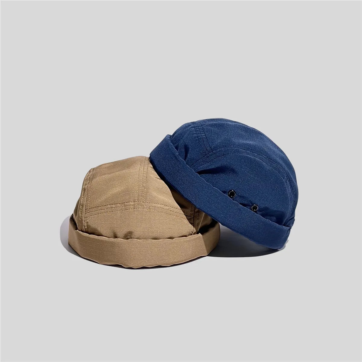 Nylon docker caps in khaki and blue leaning together, with two black eyelets visible on the blue side panel.