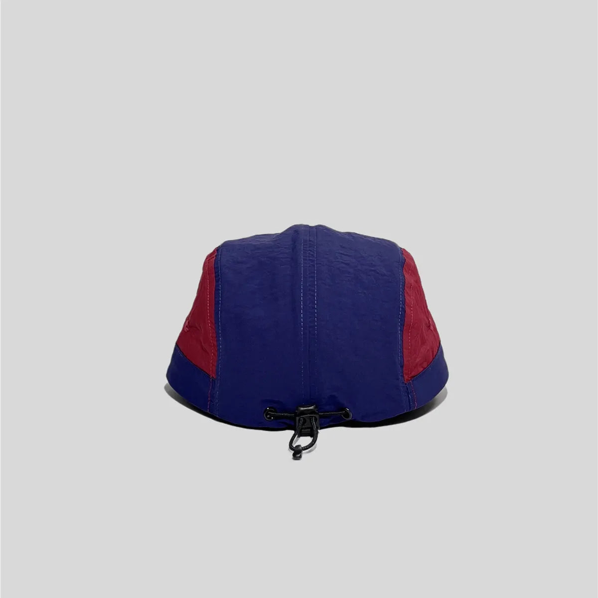 Nylon five panel cap in navy and burgundy, rear view showing the black bungee toggle and panel stitching