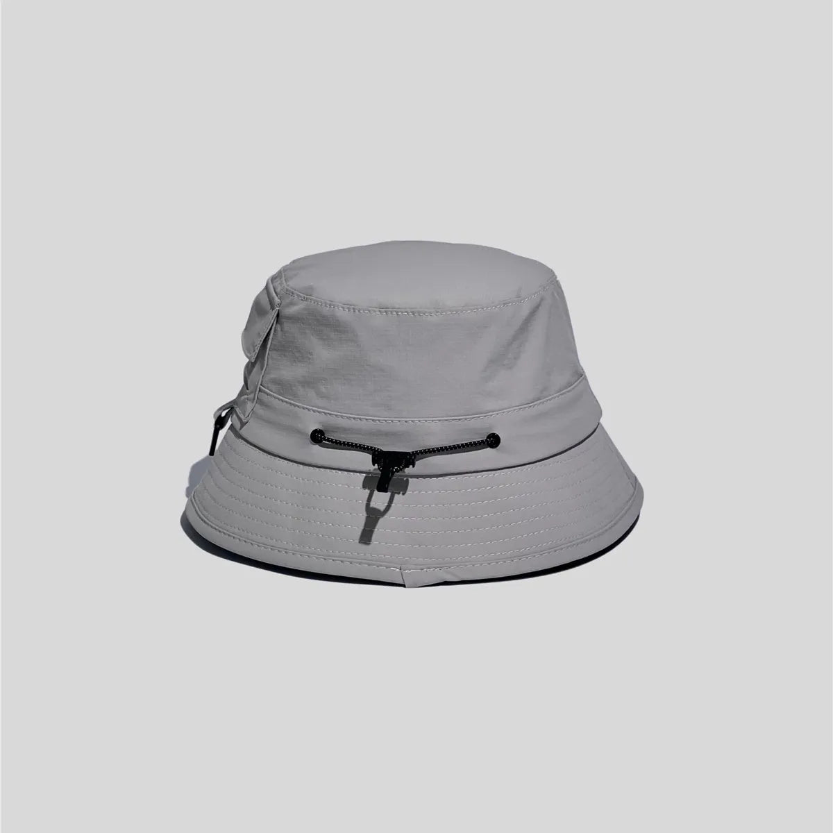 Nylon outdoor bucket hat in light grey, cord-side view showing the adjustable crown cord and multi-row brim stitching