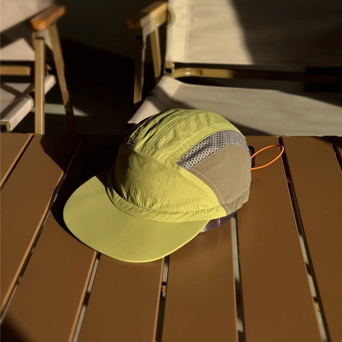 Nylon running cap in lime green and khaki on a sunlit table, with grey mesh inserts and an orange rear drawcord.